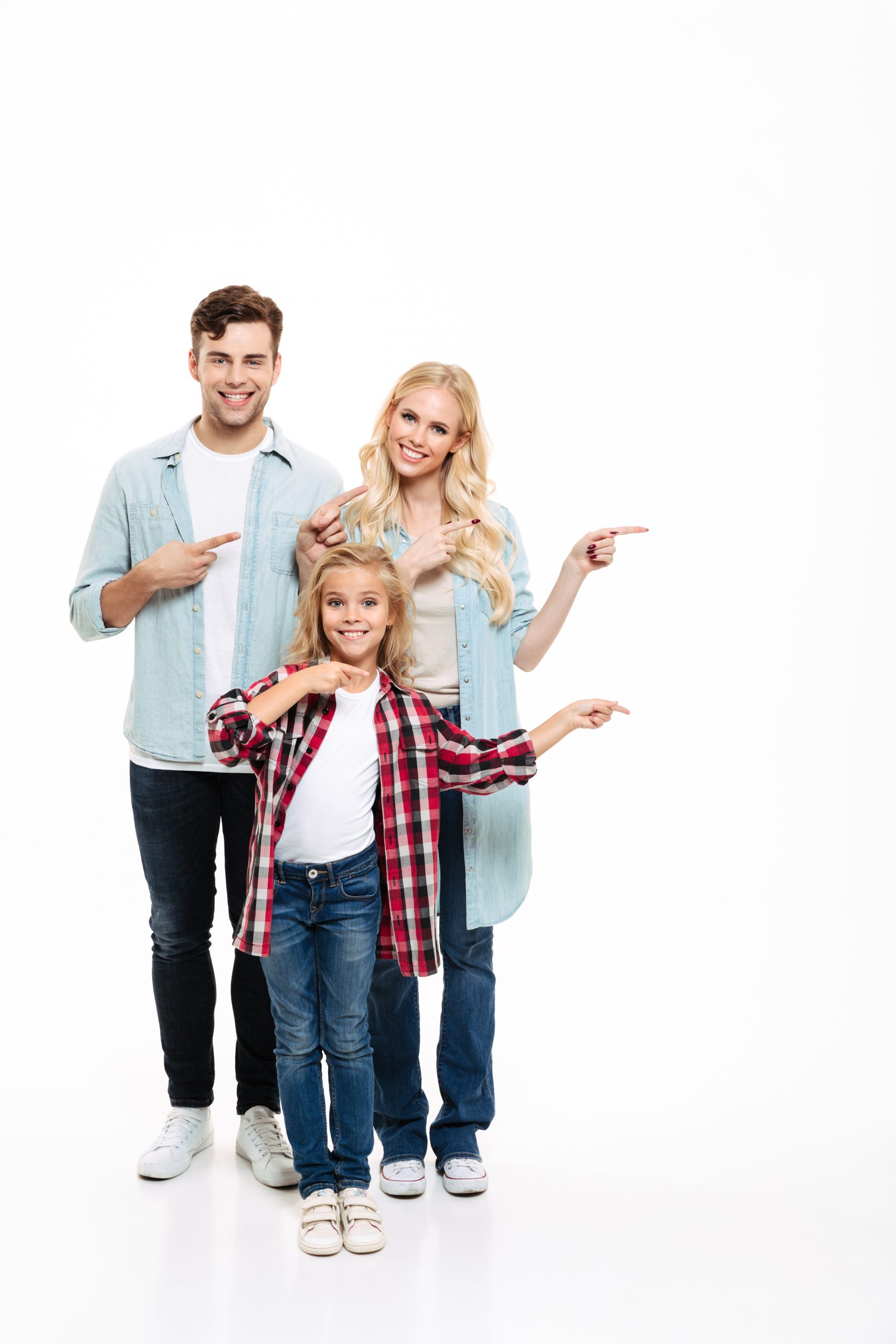 Full length portrait of a cheerful young family with a child standing together and pointing fingers away at copy space isolated over white background