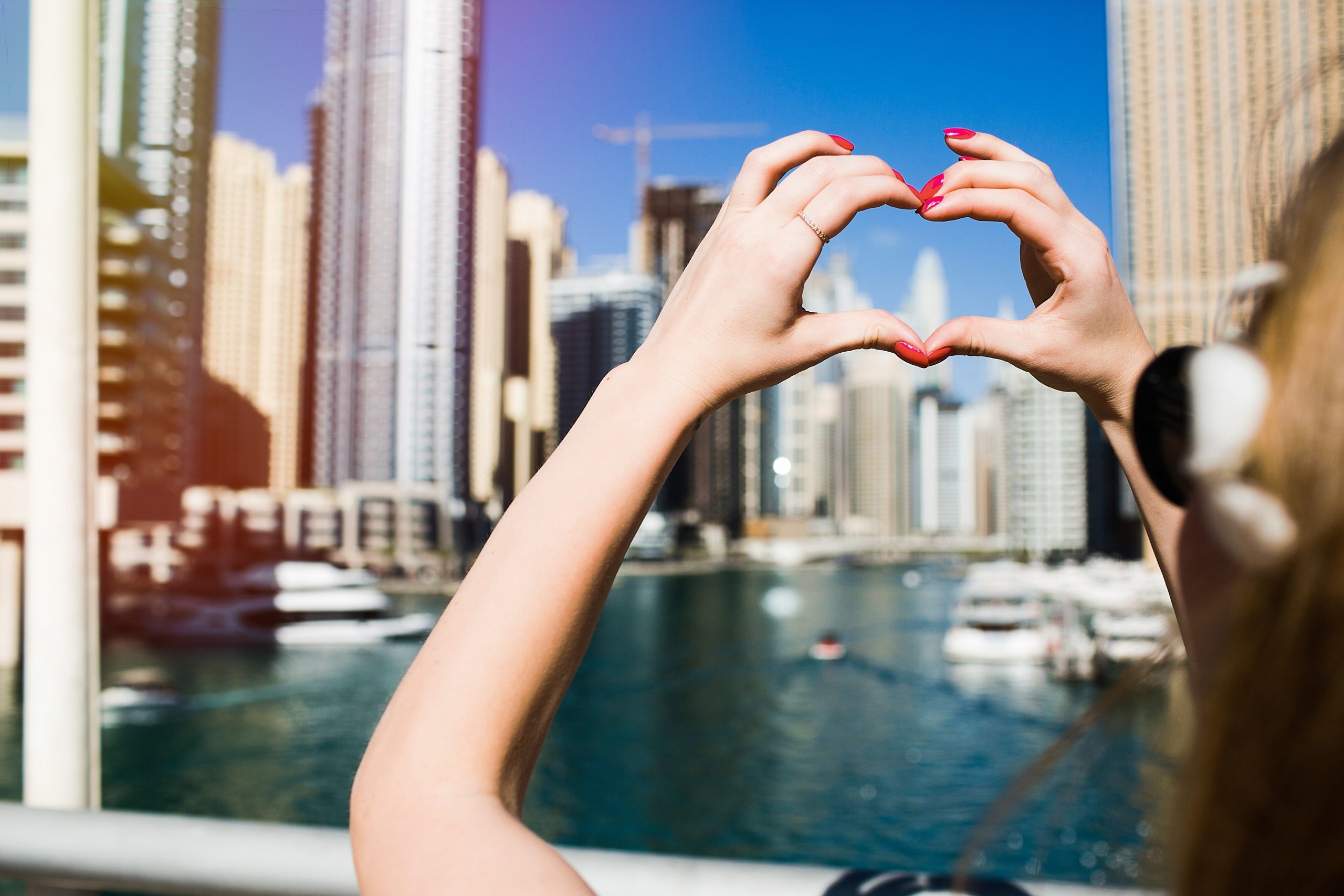 Lady with red nails shows heart with her fingers before skyscrapers of Dubai